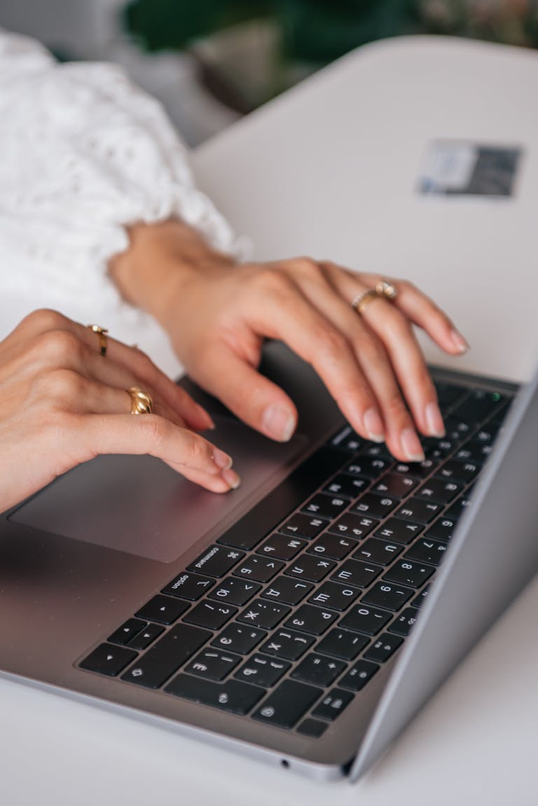 Dłonie kobiety piszącej na klawiaturze laptopa w pomieszczeniu, prezentujące pierścionki i modę, z naciskiem na to, jak pisać artykuły.