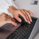 Dłonie kobiety piszącej na klawiaturze laptopa w pomieszczeniu, prezentujące pierścionki i modę, z naciskiem na to, jak pisać artykuły.