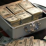 Otwarta walizka wypełniona plikami banknotów studolarowych stojąca na szklanym stole, symbolizująca bogactwo, korzyści z SEO oraz odpowiadająca na pytanie: Czym jest SEO.